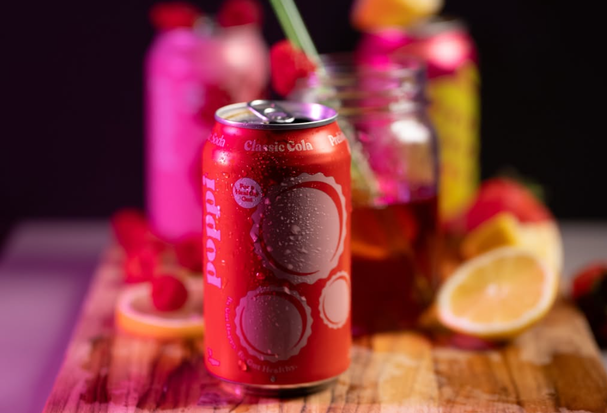 Pink raspberry drinks with citrus garnish displayed on wooden serving board. poppi drink poppi