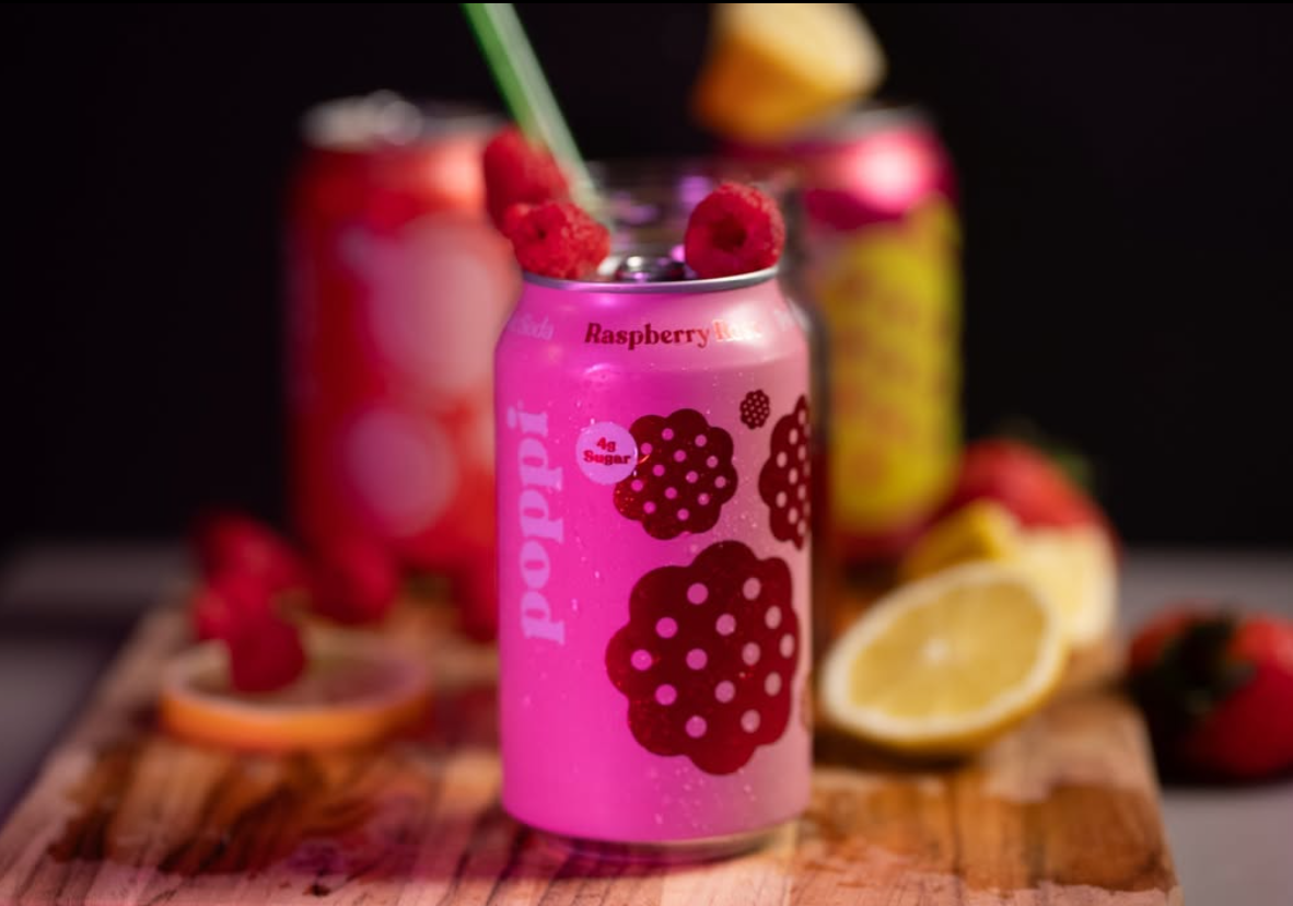 Vibrant pink raspberry drinks and fresh citrus slices on rustic wooden surface. poppi