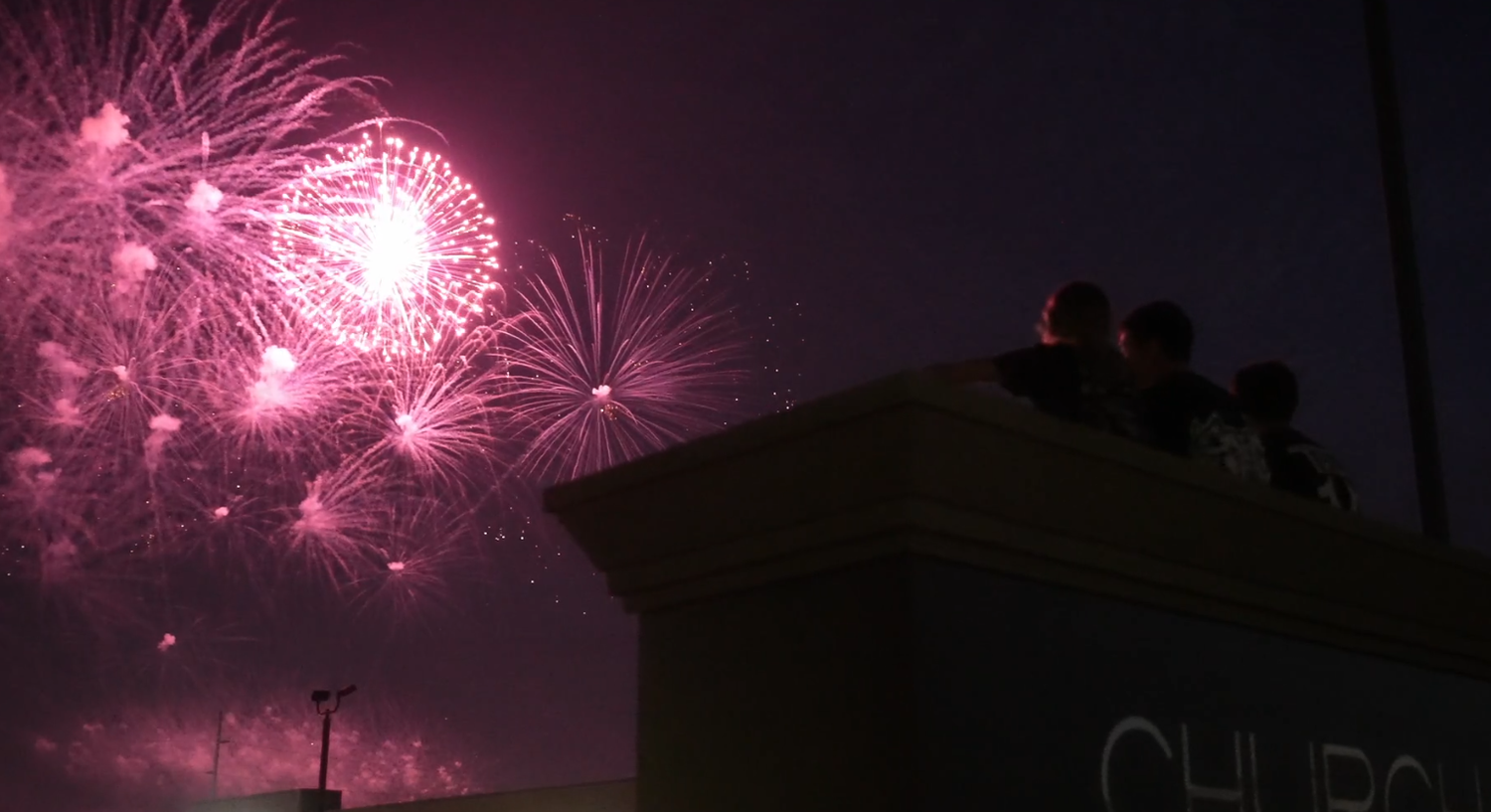 Pink fireworks display illuminating night sky with silhouettes watching from rooftop. church 321. church 3twentyone. fourth of july.