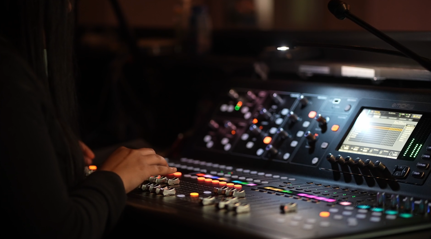 Audio mixing console in dark setting with hands adjusting controls.
music producer. music mixer. live audio.