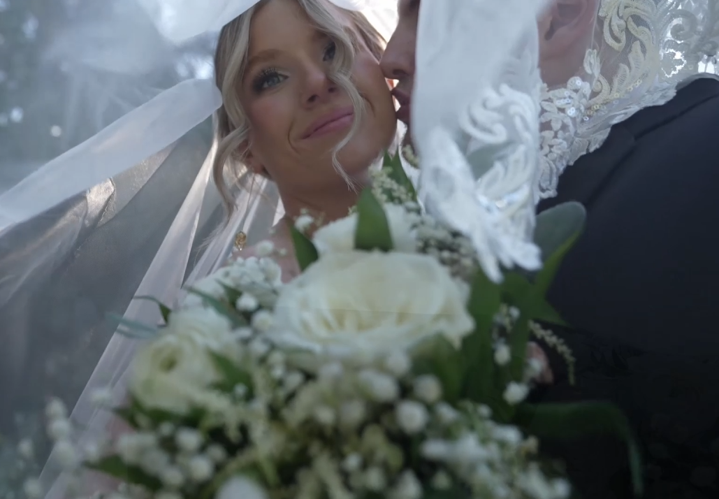 Elegant bridal bouquet with white roses seen through delicate lace veil.