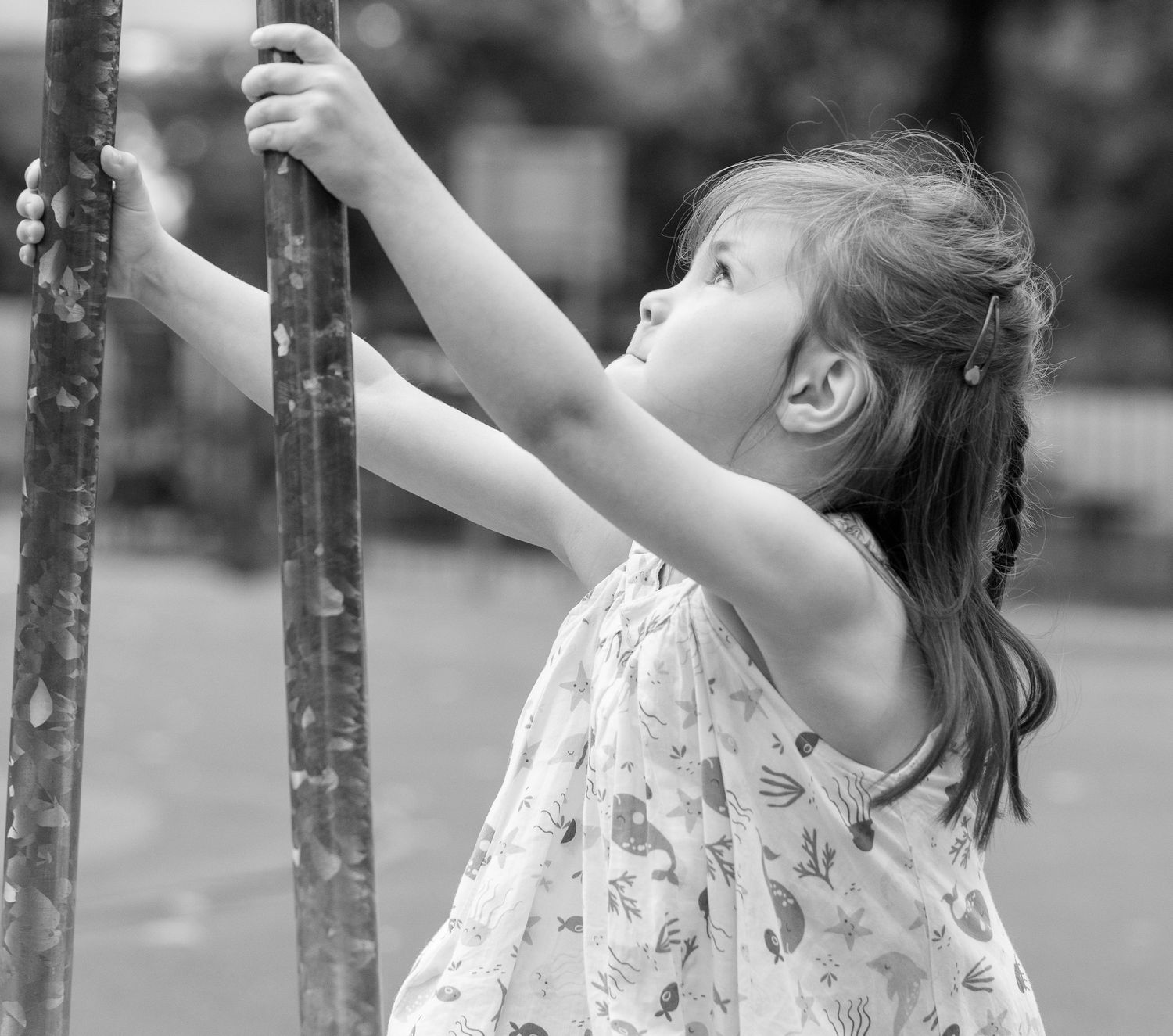 A child reaches up to grab playground equipment in a flowing dress.