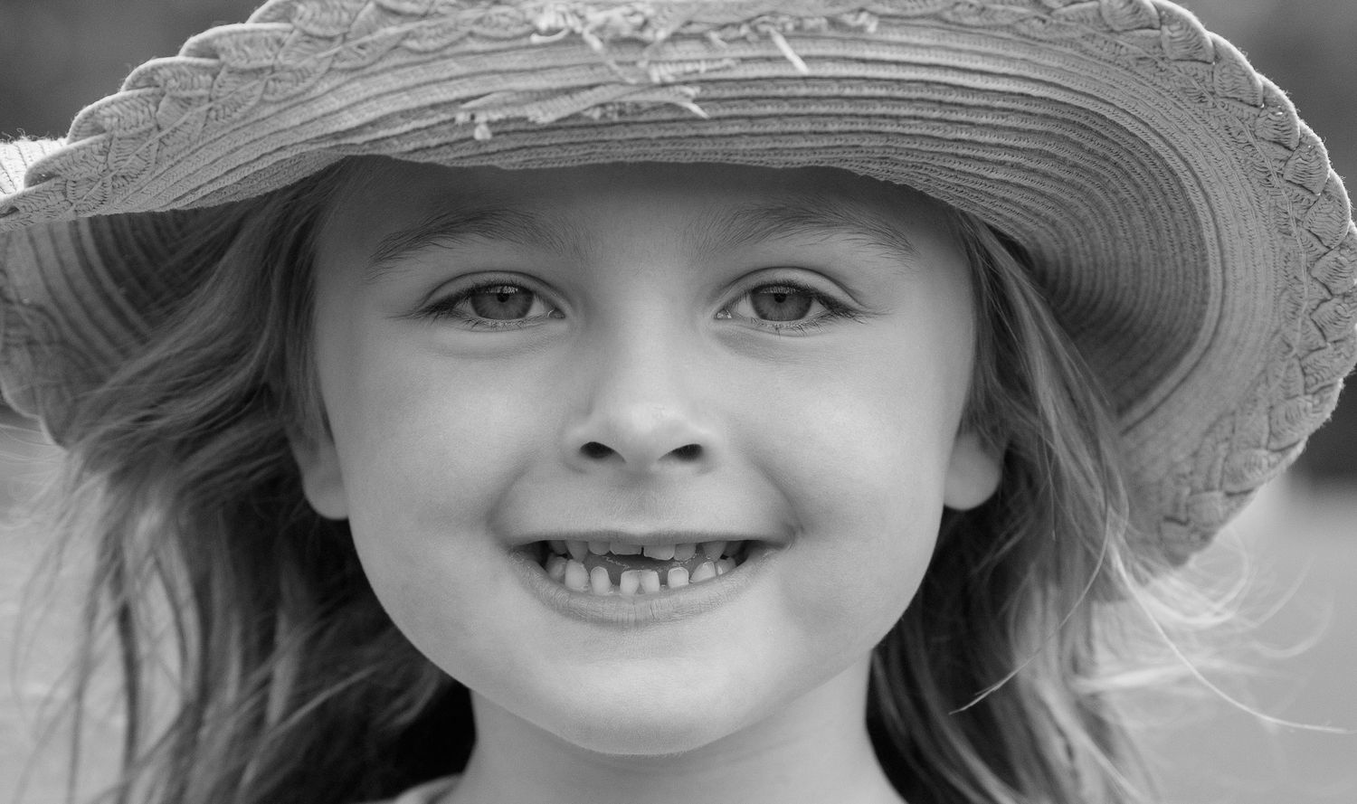 Black and white portrait of a young child wearing a sun hat with a joyful expression.