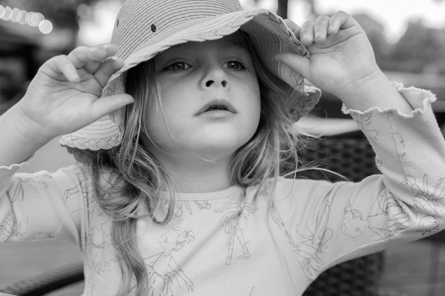 Black and white image of a young child adjusting a sun hat while looking upward.