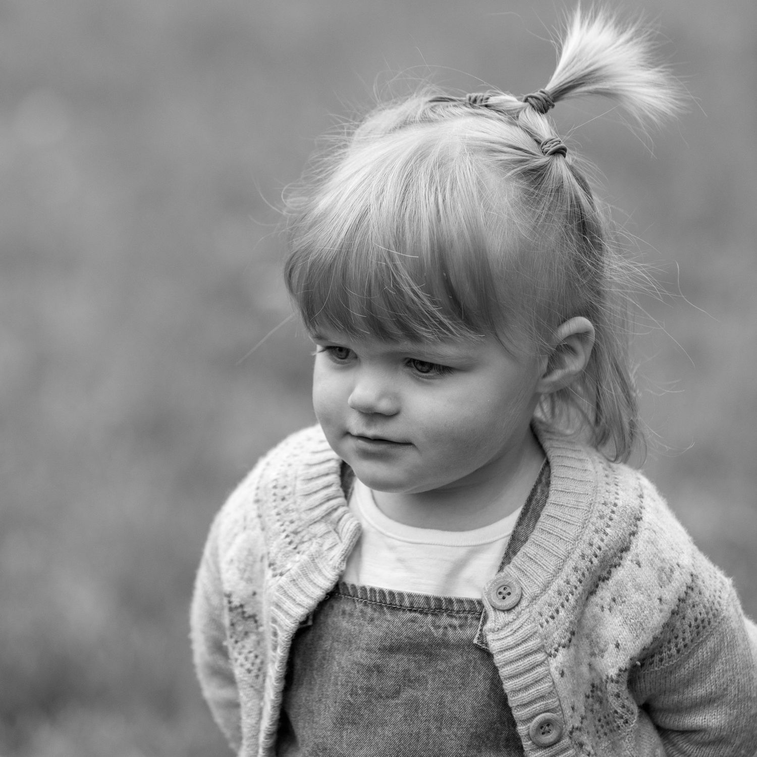 A black and white photo series showing a young child in a knit cardigan with different expressions and poses.