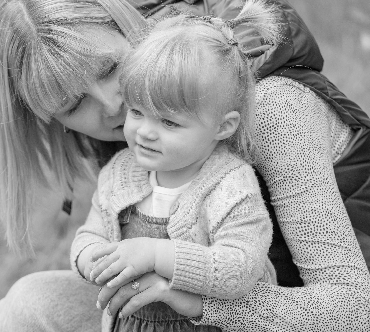 A tender black and white portrait showing an intimate moment between parent and child in cozy sweaters.