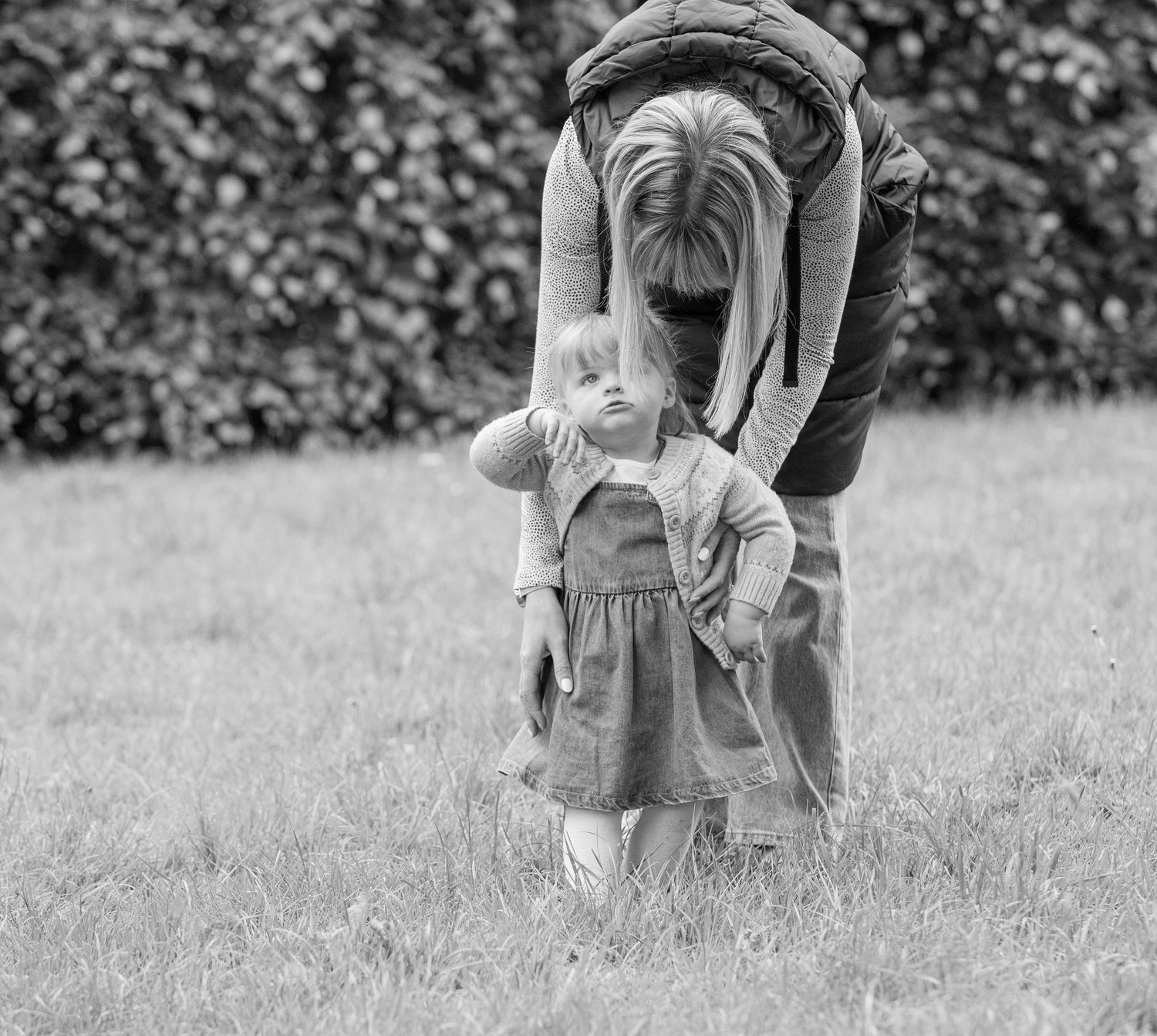 Parent and child playing peek-a-boo game in a garden setting.
