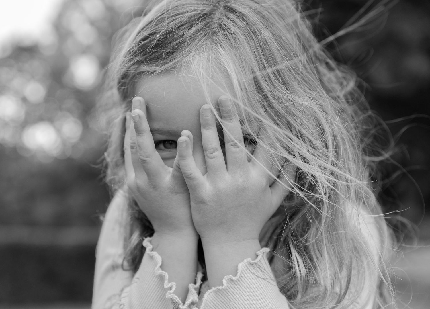 Black and white photo of a child peeking through fingers while playing peek-a-boo.