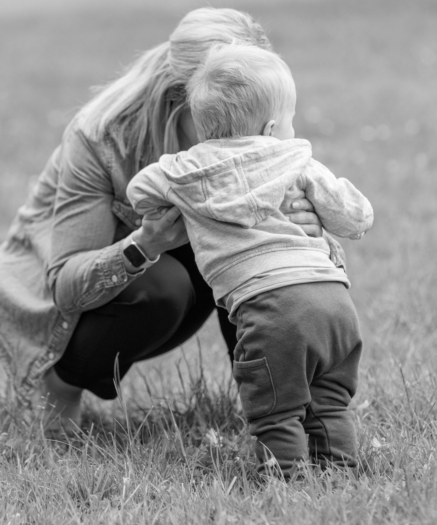 Black and white photo of a tender moment between adult and child outdoors in the grass.