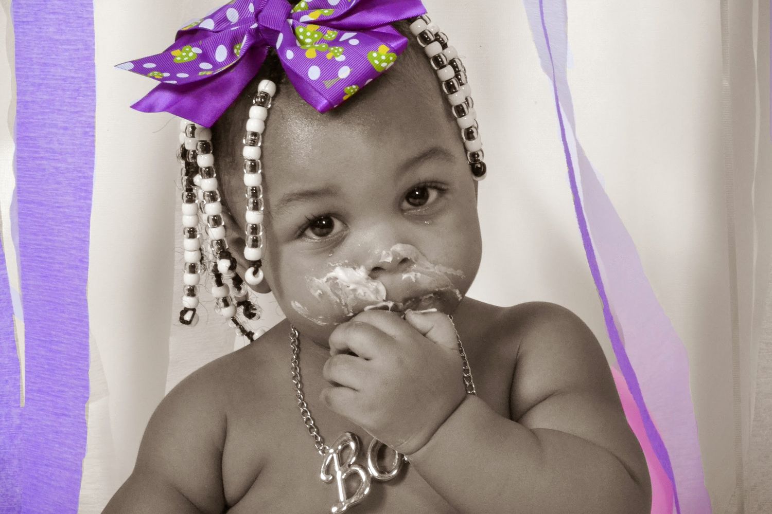 A baby girl with braids and a purple bow headband eats cake during her first birthday photo shoot.