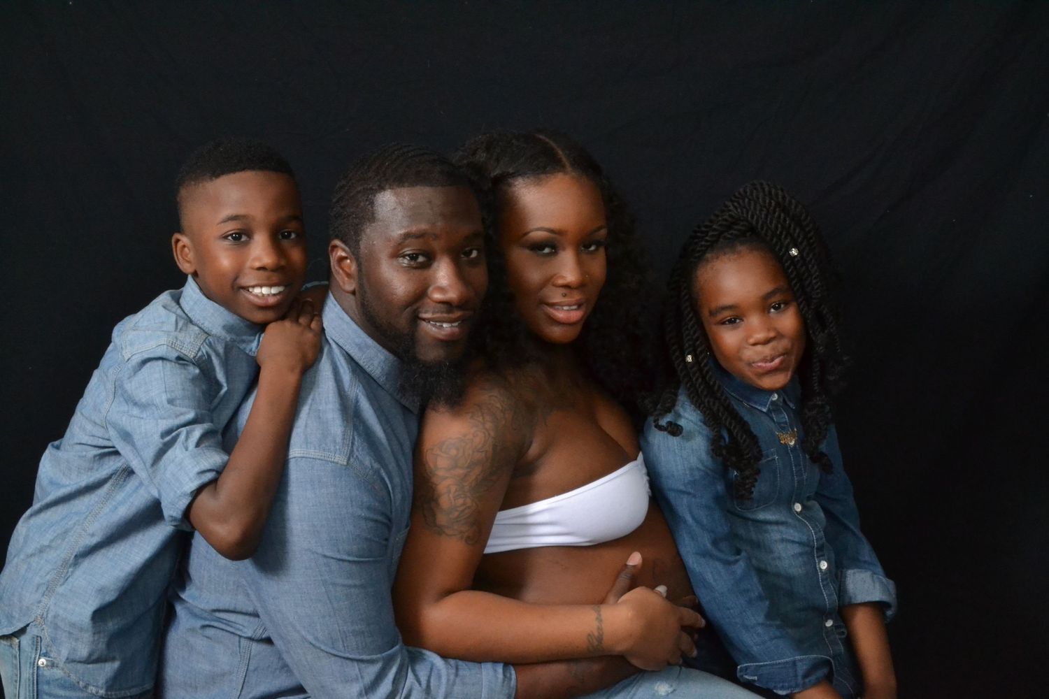 Smiling family of four in denim outfits posing together against a dark background in a professional studio photo.