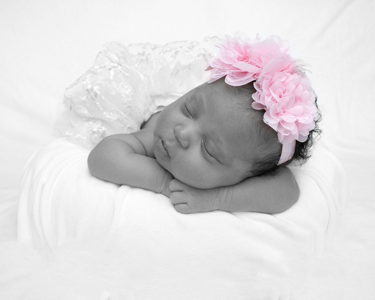 Sleeping newborn baby girl wearing a pink flower headband, black and white photo with soft white blanket.