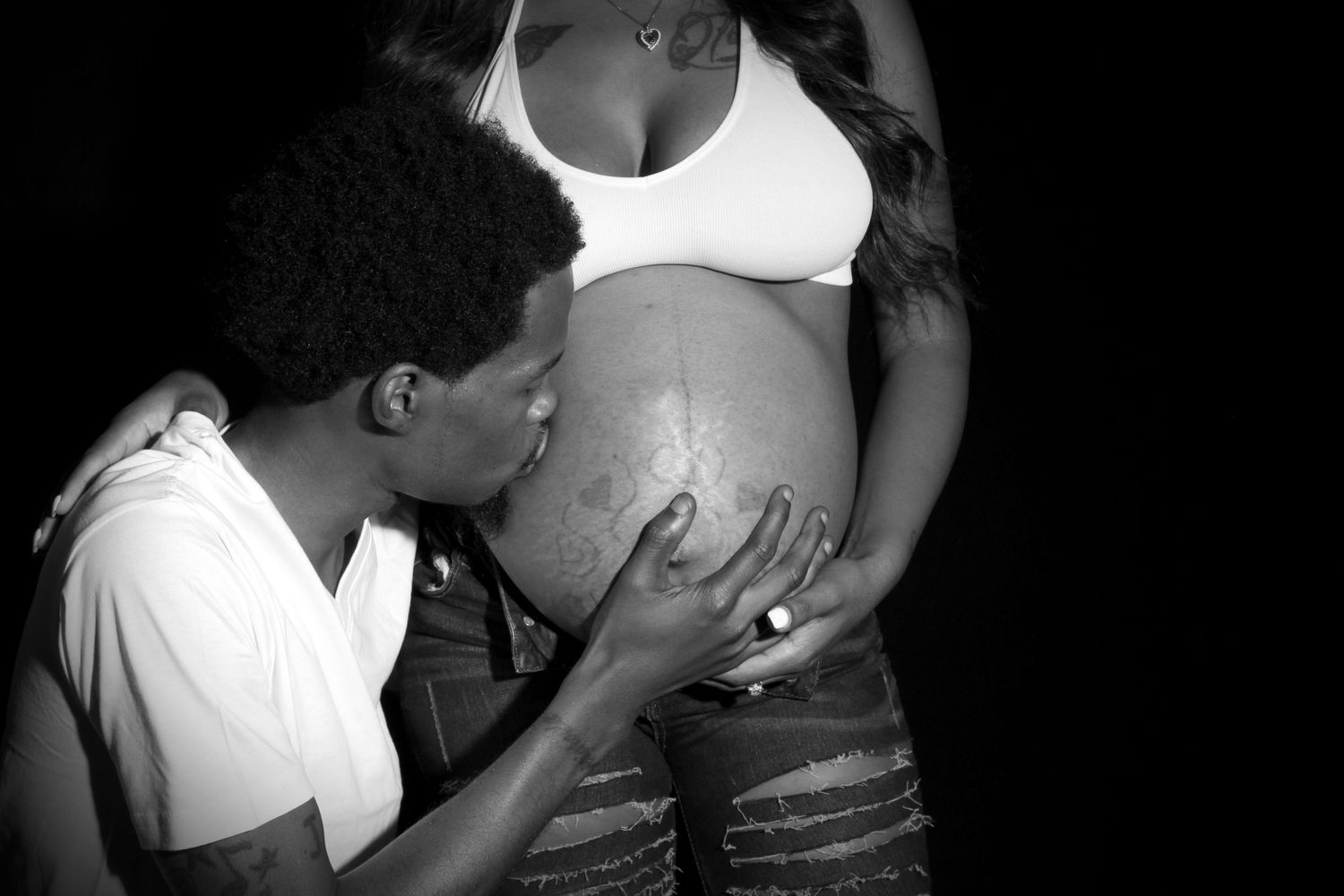 Black and white maternity photo of a man kissing a pregnant woman's belly during a couples photoshoot.