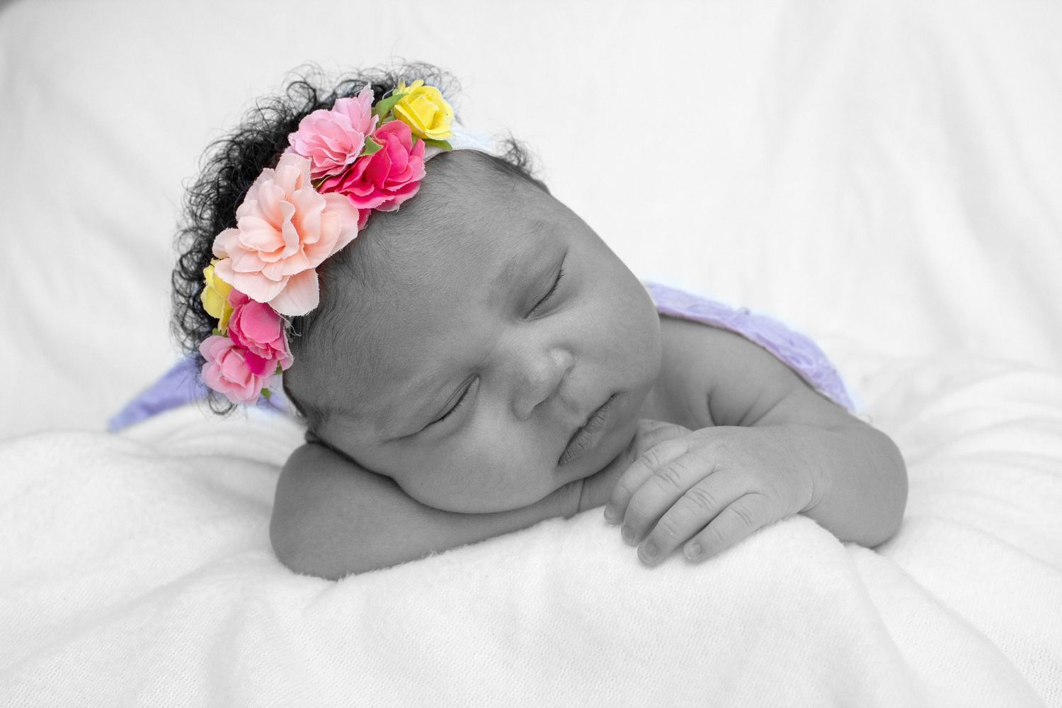 Black and white photo of sleeping newborn baby wearing colorful flower crown headband.