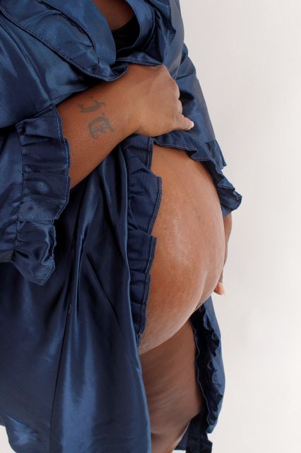 Close-up of a pregnant woman in a navy blue satin robe revealing her bare baby bump.