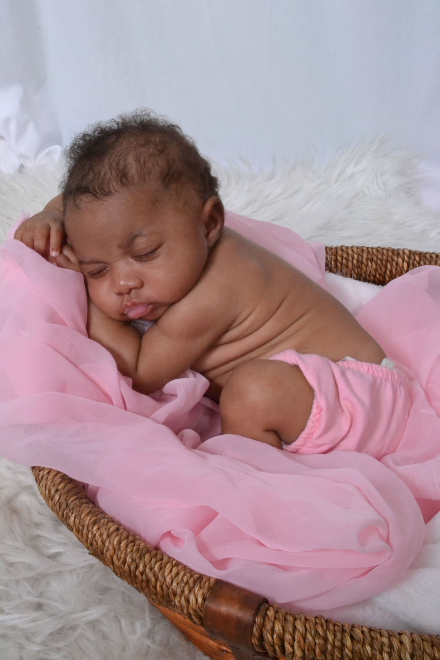 Sleeping newborn baby girl wrapped in pink fabric resting in a wicker basket with fur lining.
