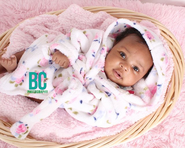 Newborn baby in floral outfit lying in wicker basket on pink blanket, professional BC Photography portrait.