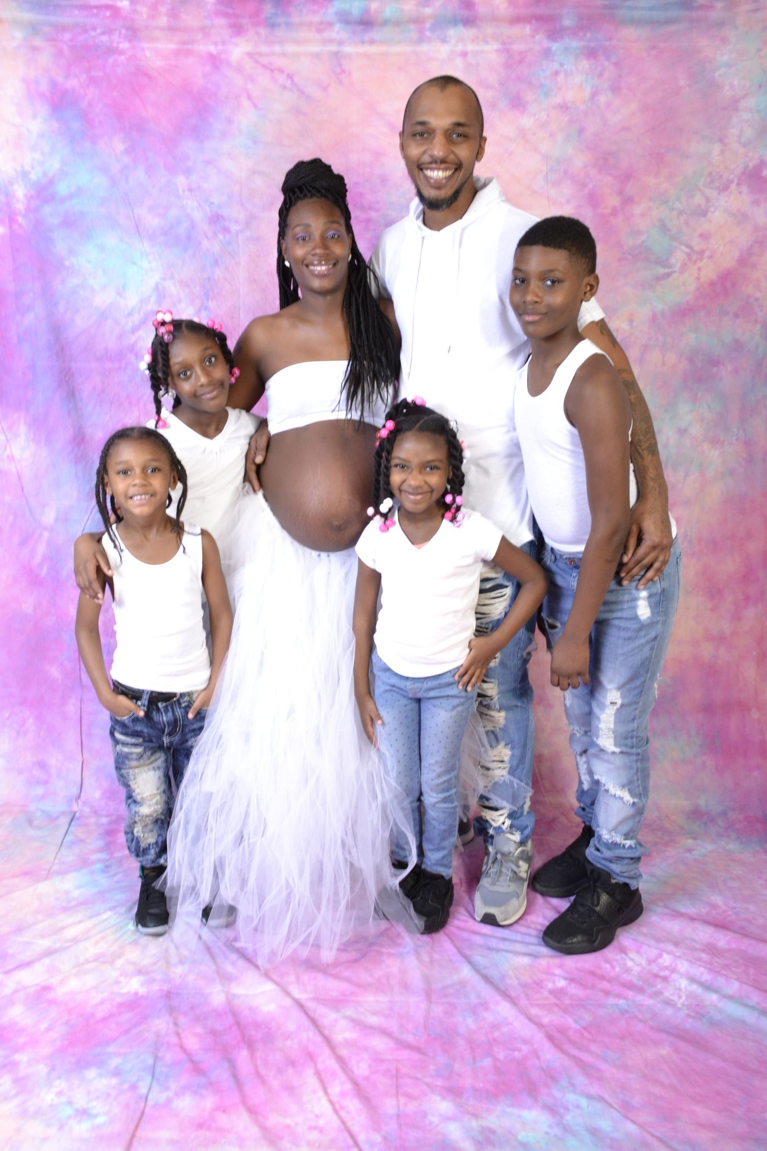 Happy family of six in white outfits poses together with pregnant mother against colorful backdrop.