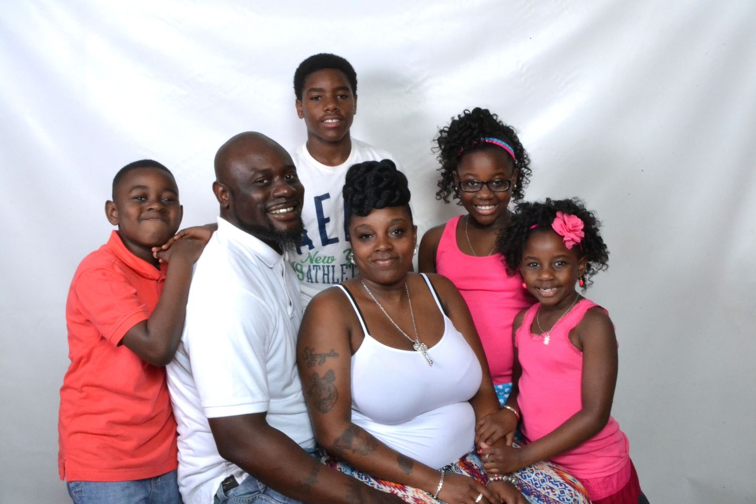Family of six poses together for portrait, with parents and four children against white backdrop.