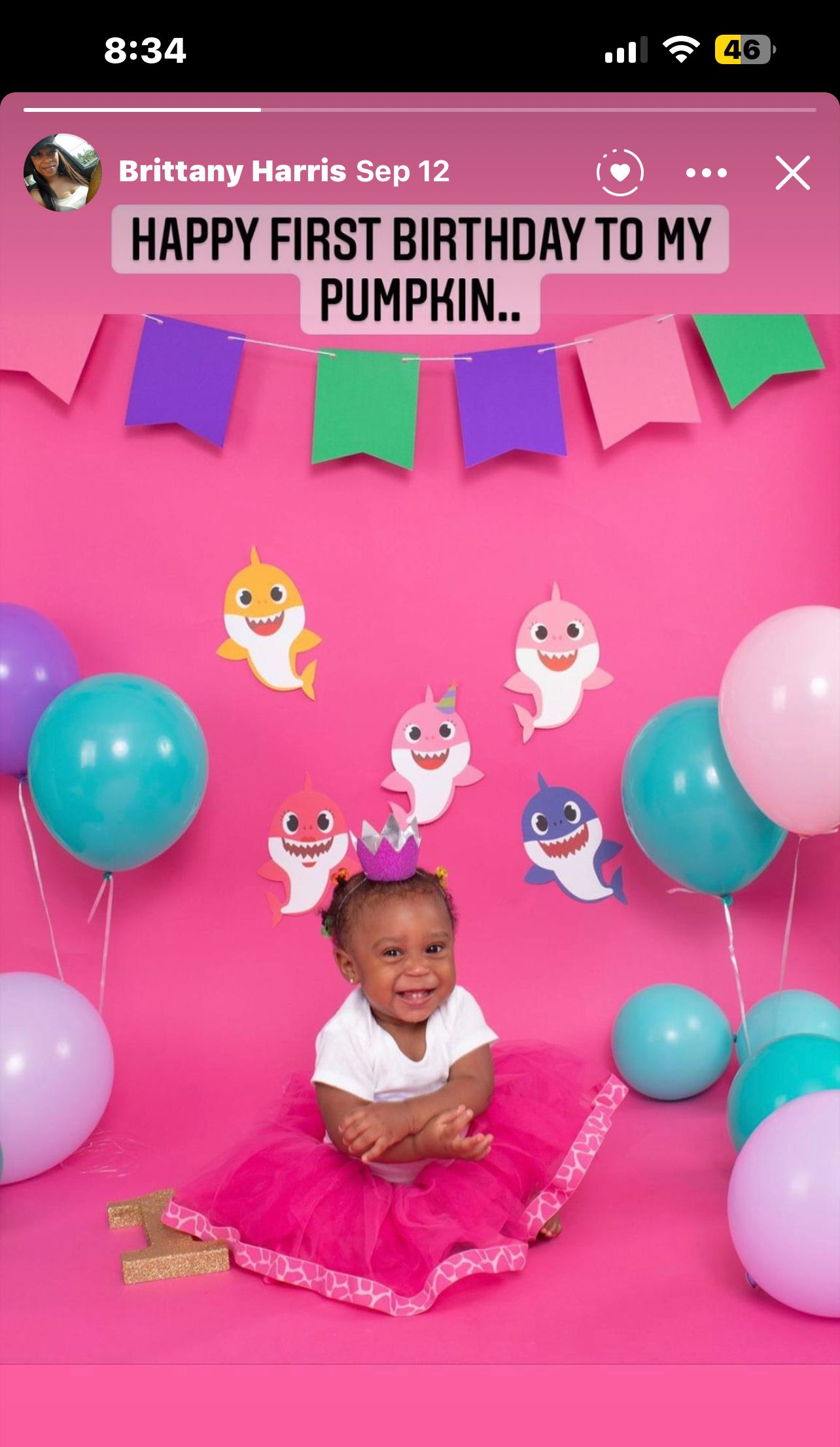A baby celebrates her first birthday with a Baby Shark themed pink party setup.