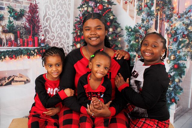 A mother and three children wear matching red plaid Christmas pajamas in a festive holiday portrait.