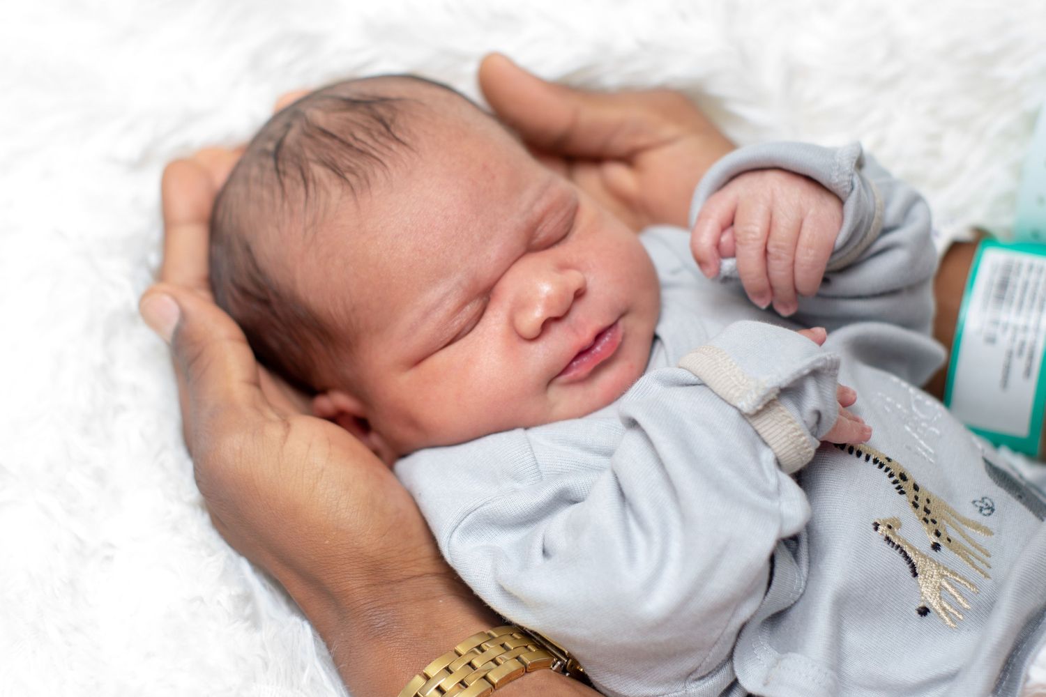 Newborn baby in gray outfit sleeping peacefully in parent's gentle hands.