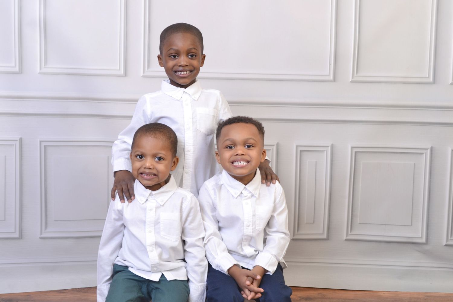 Three young brothers in white button-up shirts pose together for a classic studio portrait.