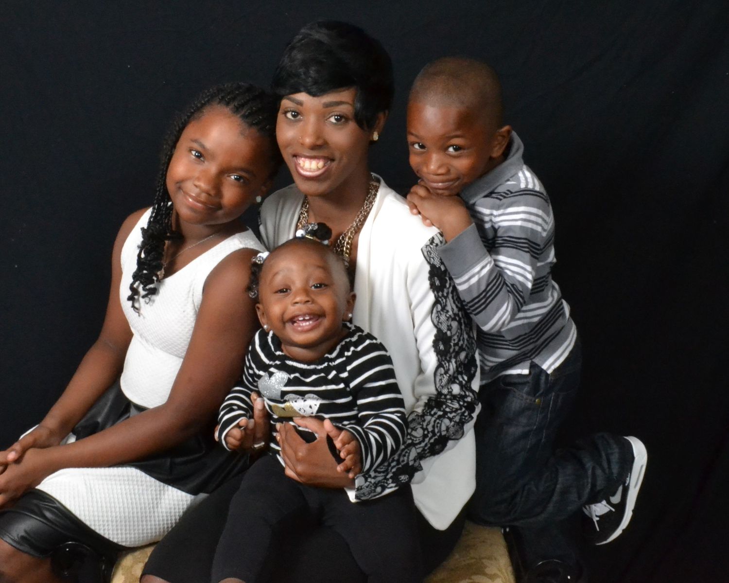 Loving mother poses with three young children in a warm professional studio family portrait against dark background.
