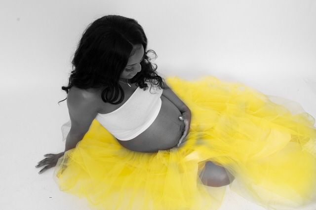 Artistic maternity photo of pregnant woman in white crop top with vibrant yellow tulle skirt in selective color.