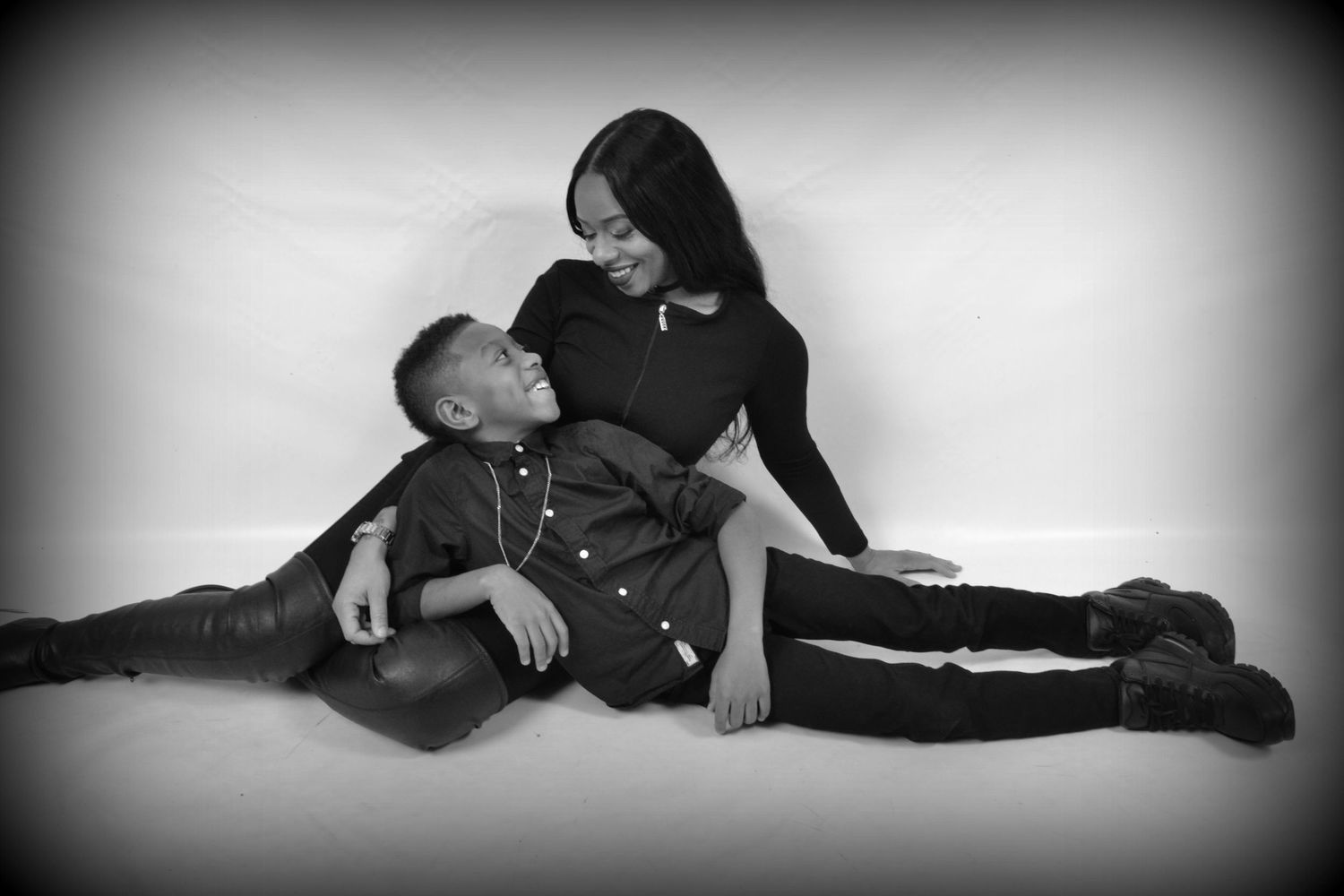 Black and white studio portrait of a mother and young son sitting together on the floor sharing a moment.