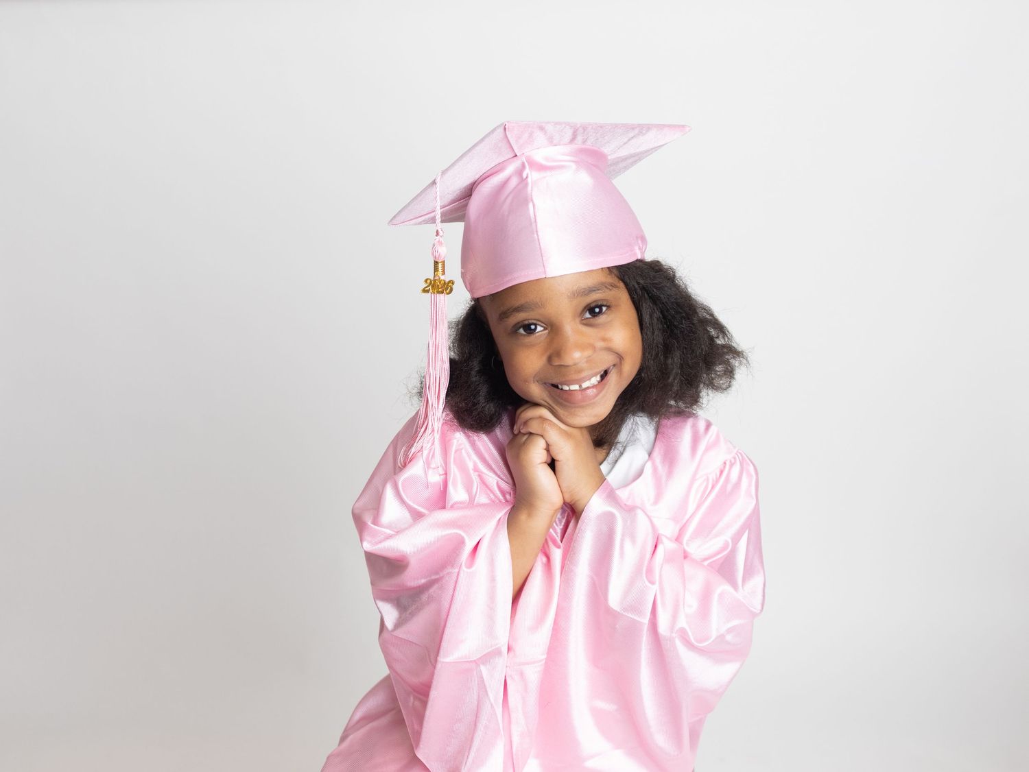 Young girl in pink graduation cap and gown smiling proudly, perfect for preschool or kindergarten graduation photos.