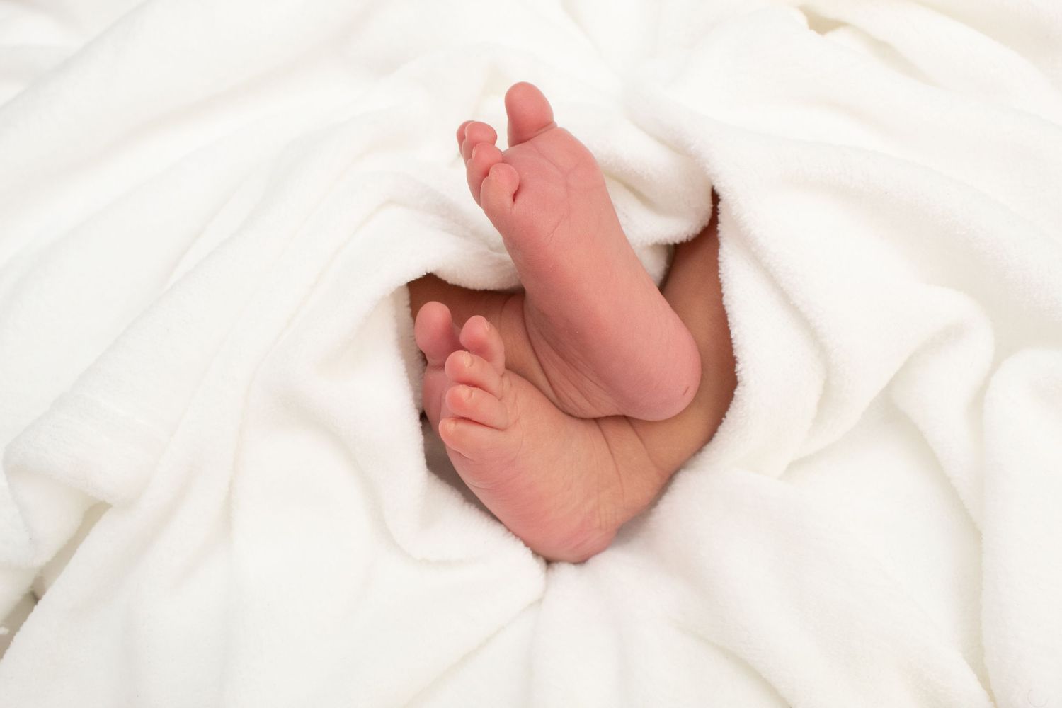 Tiny newborn baby feet peeking out from soft white blanket.