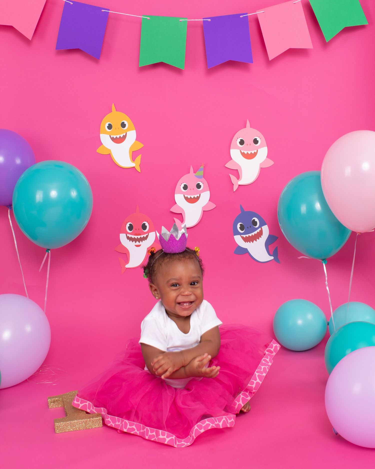 A baby in a pink tutu celebrates her first birthday with a Baby Shark themed backdrop.