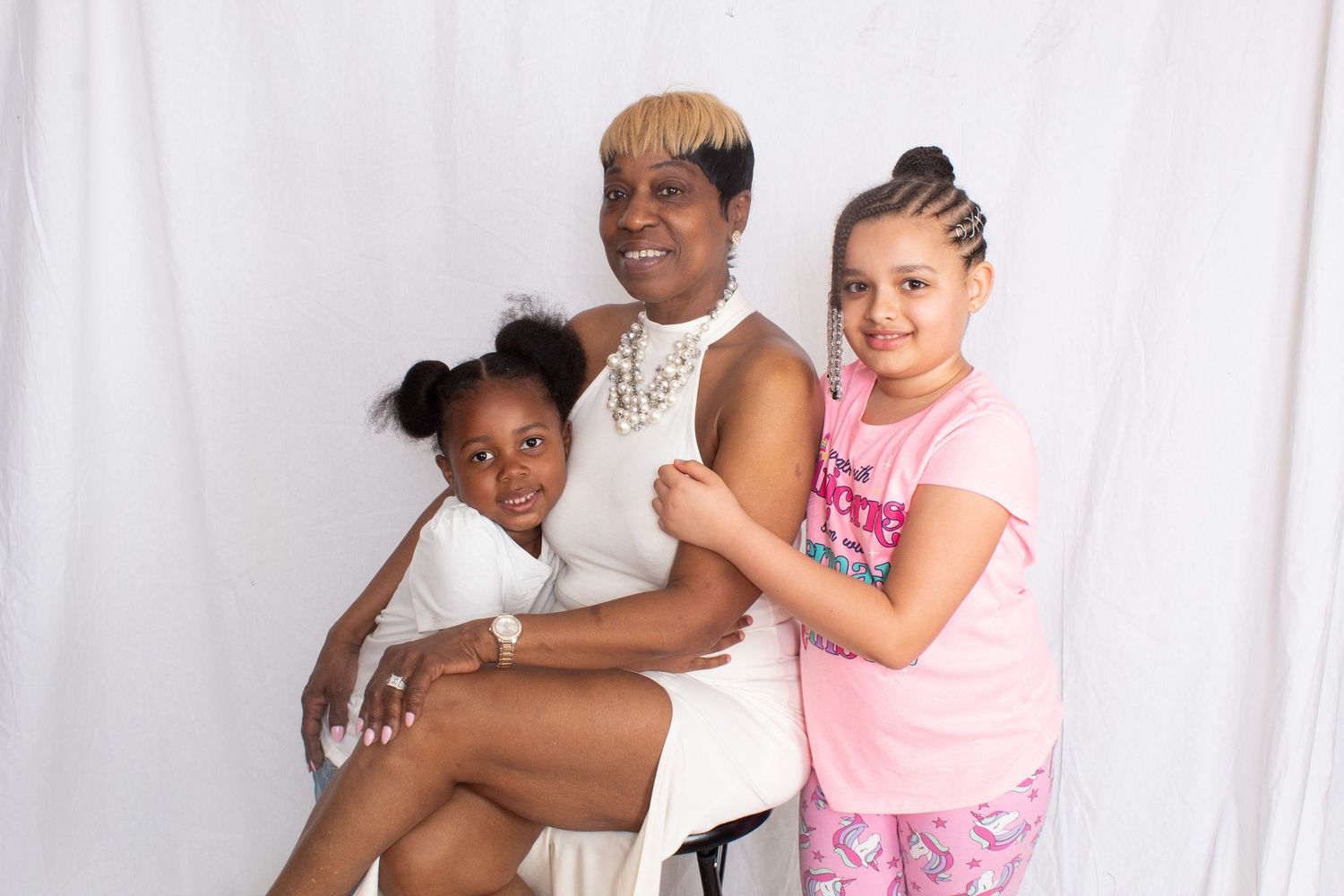 A woman sits with two young girls beside her in a casual family portrait against a white backdrop.
