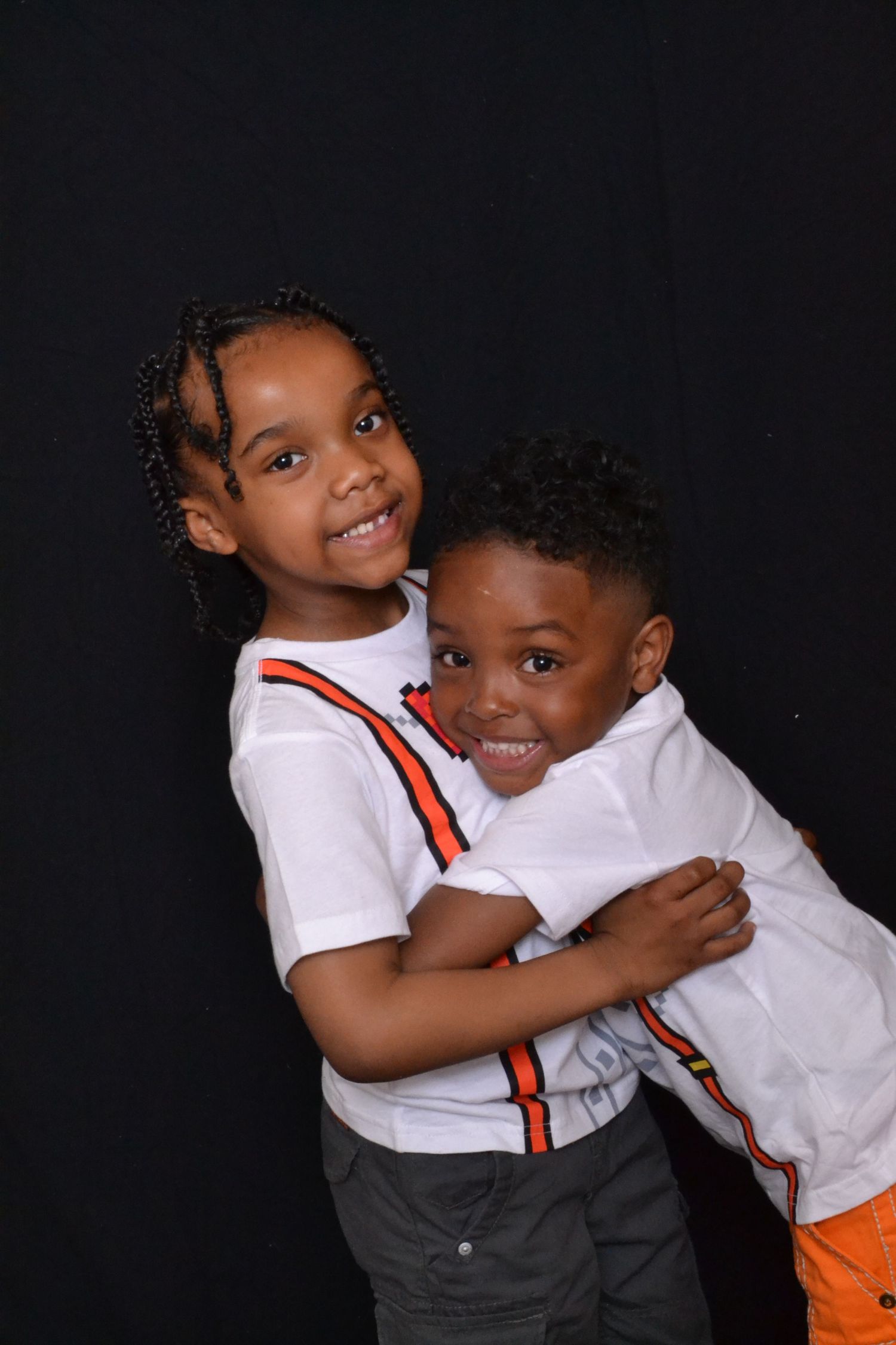 Two young brothers hugging and smiling together wearing white shirts against black background.