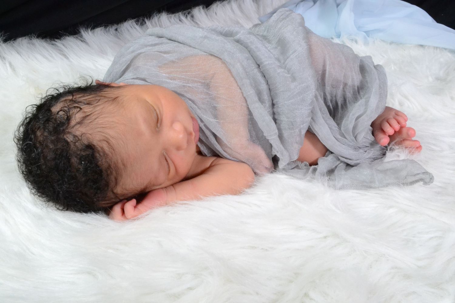 Peaceful sleeping newborn baby swaddled in gray wrap lying on white fluffy fur blanket.