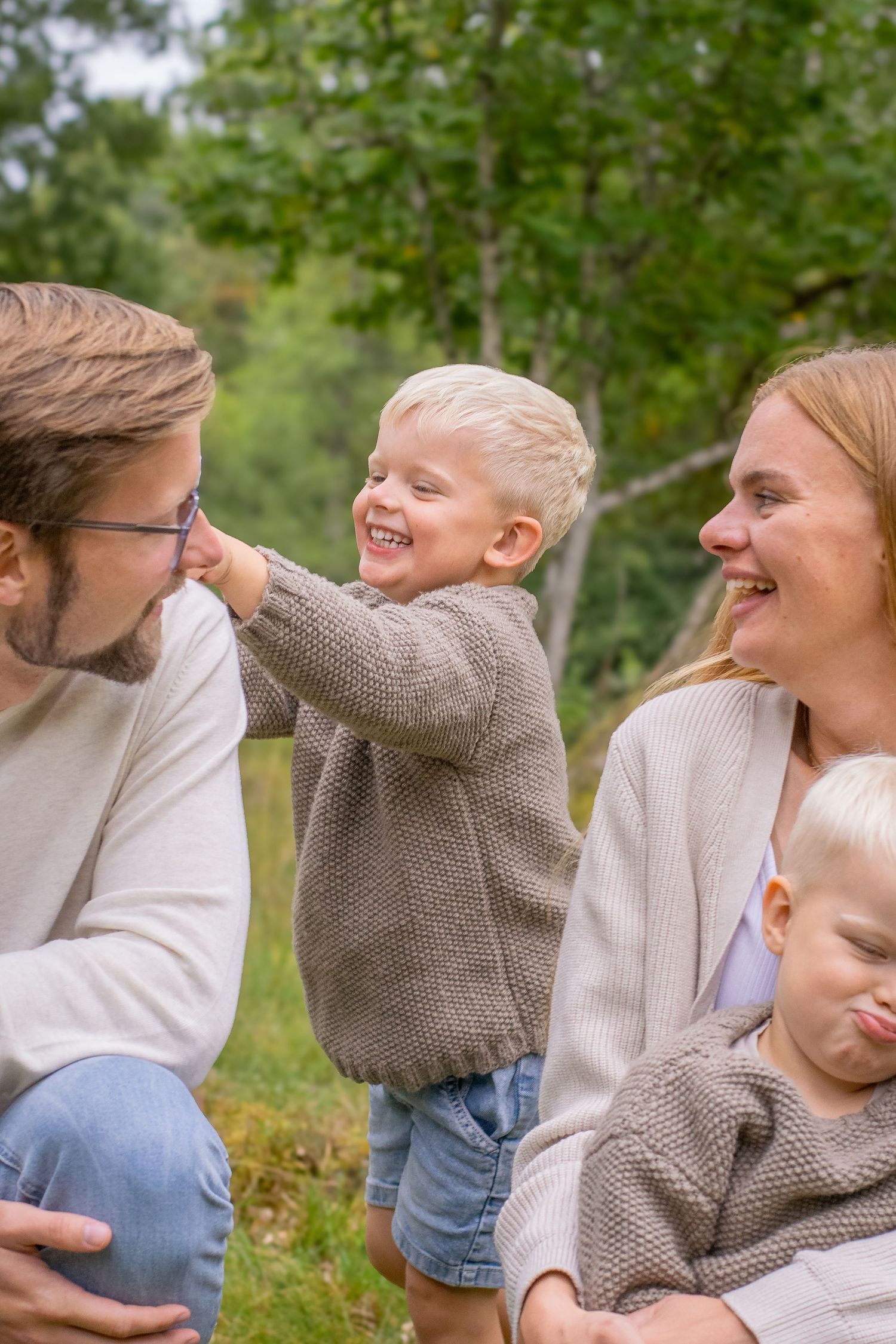 En pojke ler stort och kittlar sin pappa till vänster om sig. Hans mamma sitter till höger i bild med ett stort leende.