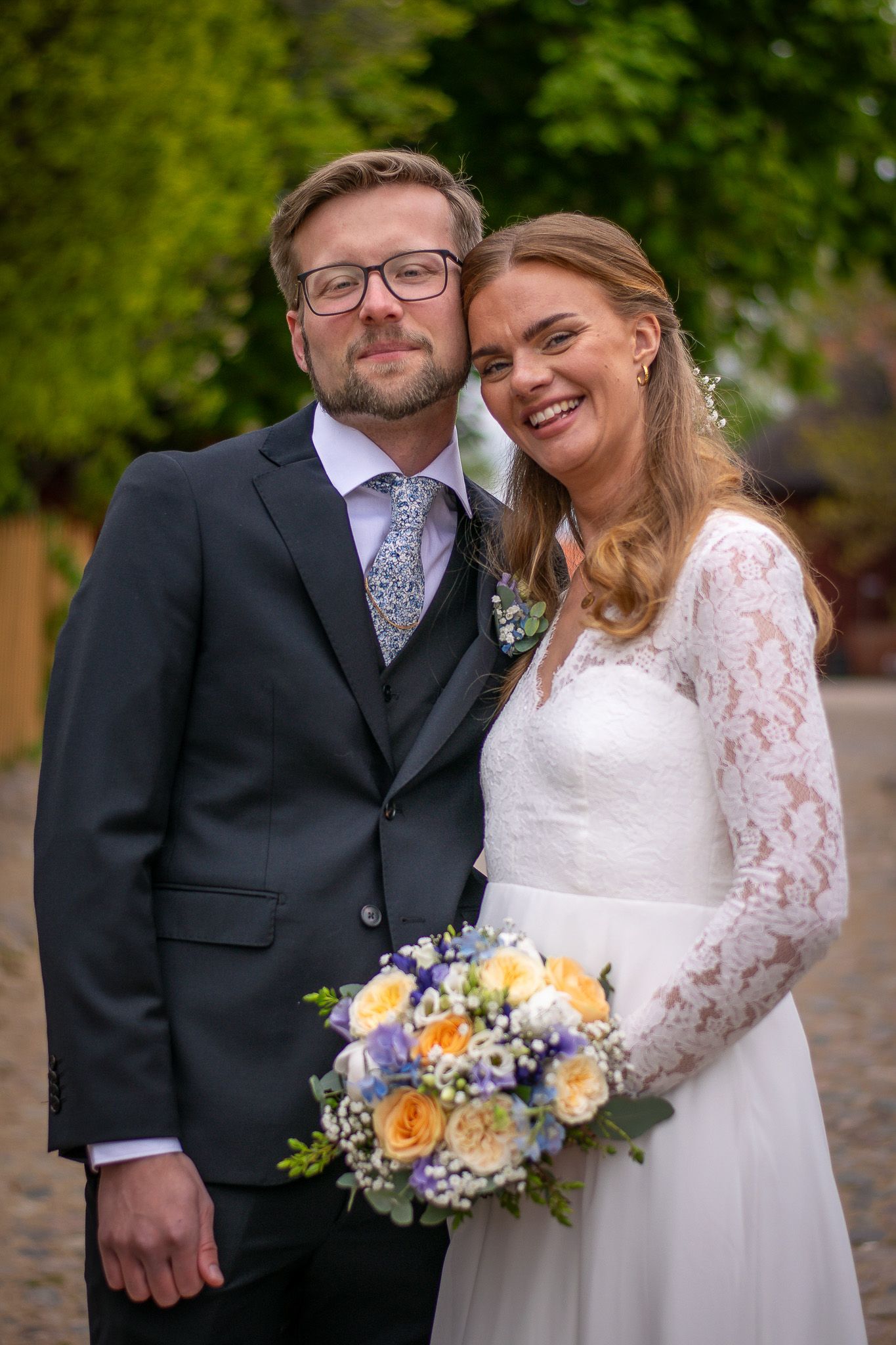 Brudpar som tittar in i kameran, med huvudena lutandes mot varandra, där båda ler och ser lyckliga ut.