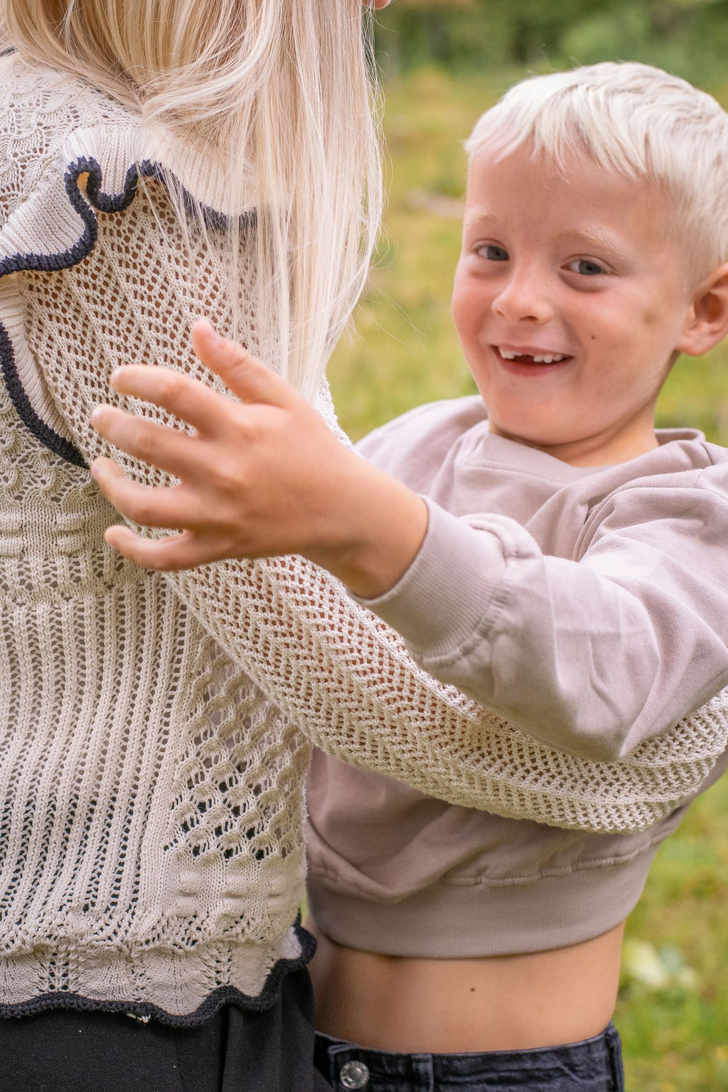 En blond pojke ler stort och tittar in i kameran, samtidigt som han håller om sin mamma.
