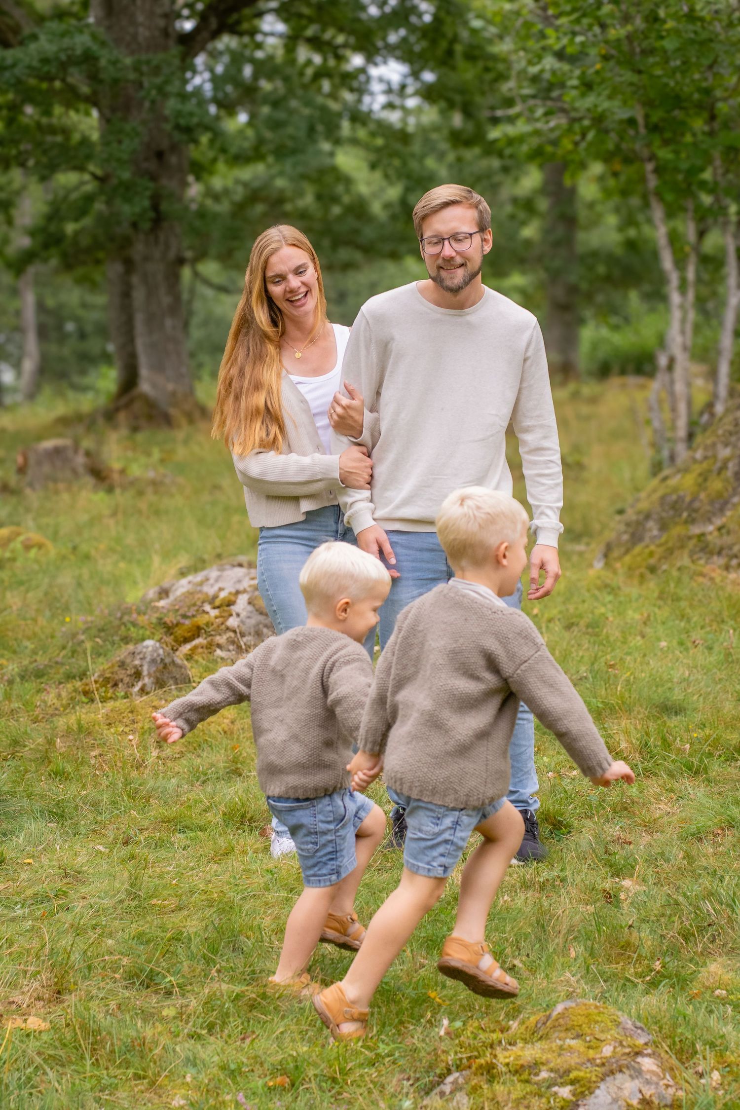 En mamma och pappa står i mitten av bilden och håller om varandra. Framför dem springer två pojkar förbi dem och håller varandra i handen.