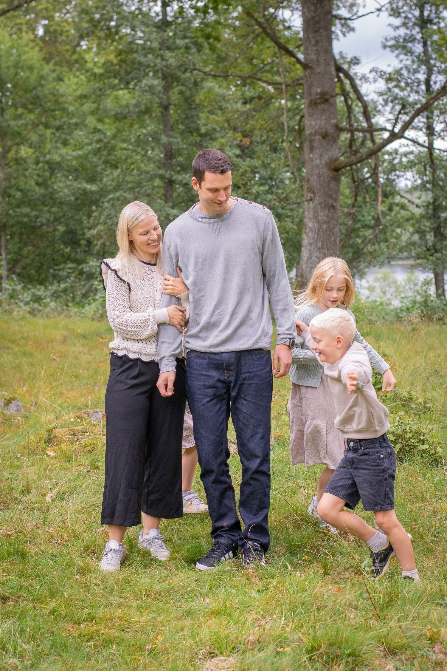 En mamma och pappa står i mitten av bilden och håller om varandra. Framför dem springer en pojke och en flicka förbi dem leendes.