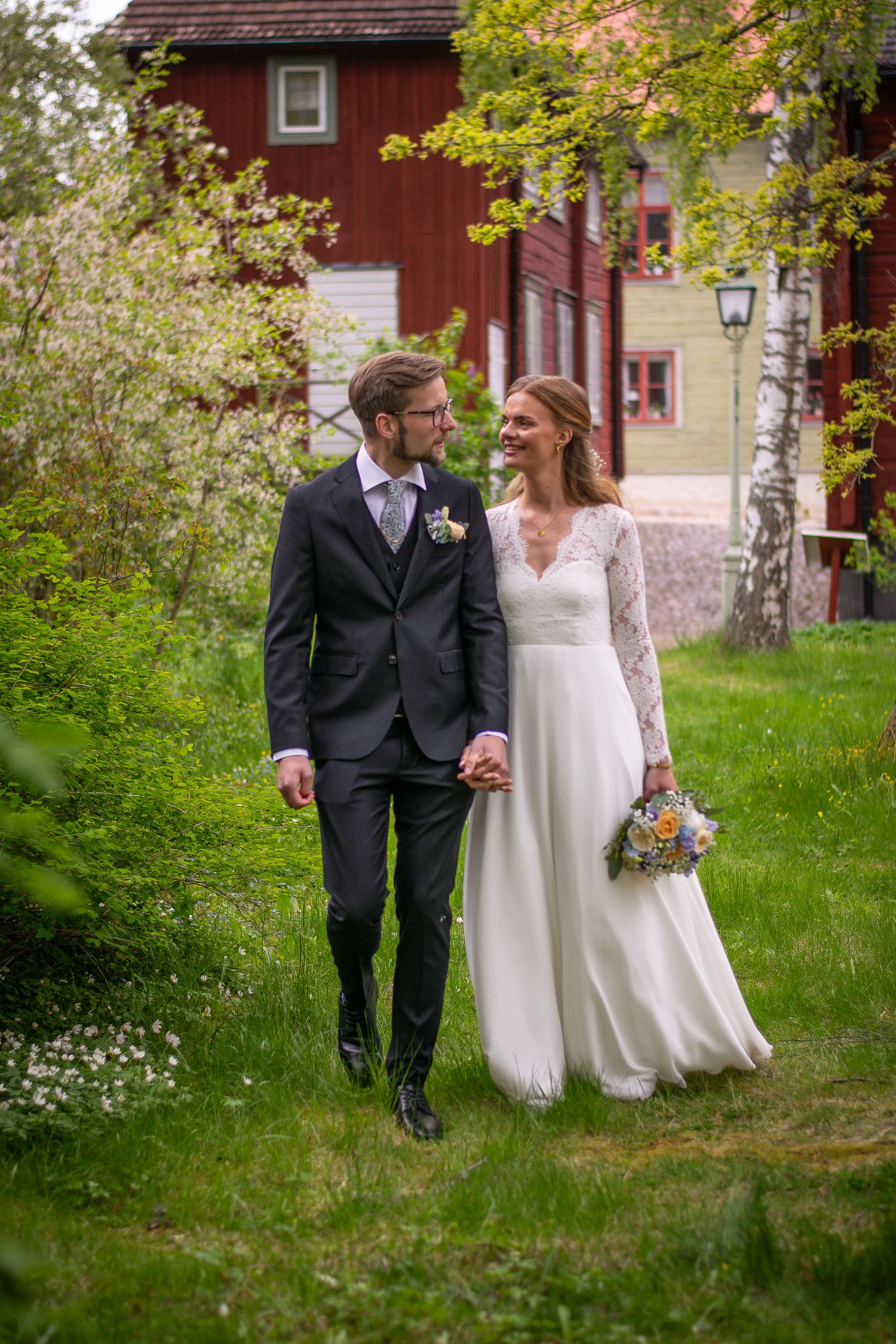 Brudpar som håller handen och går nära varandra mot kameran, medan de tittar kärleksfullt på varandra.