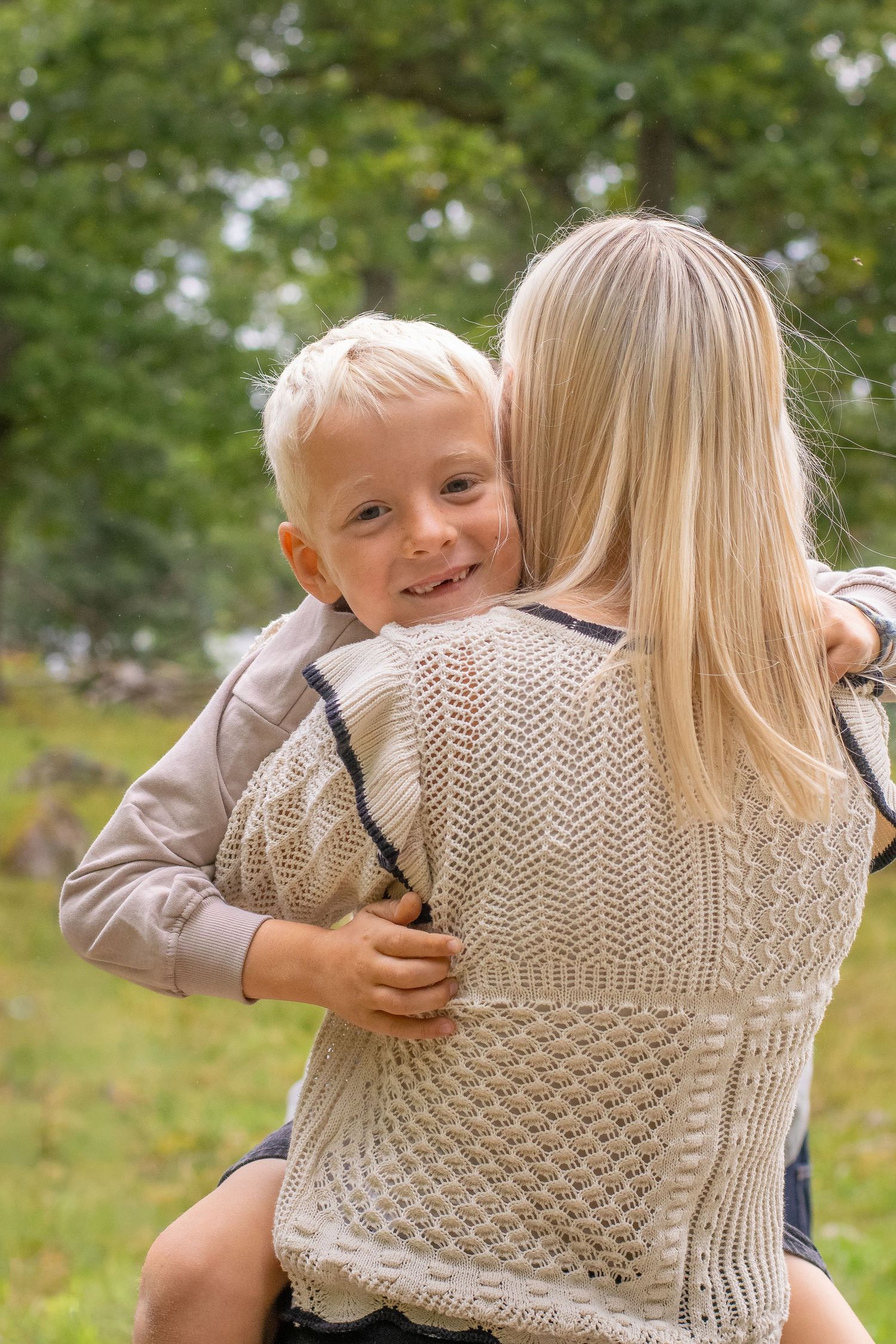En pojke är i sin mammas famn och tittar rakt in i kameran med mammans rygg mot kameran.