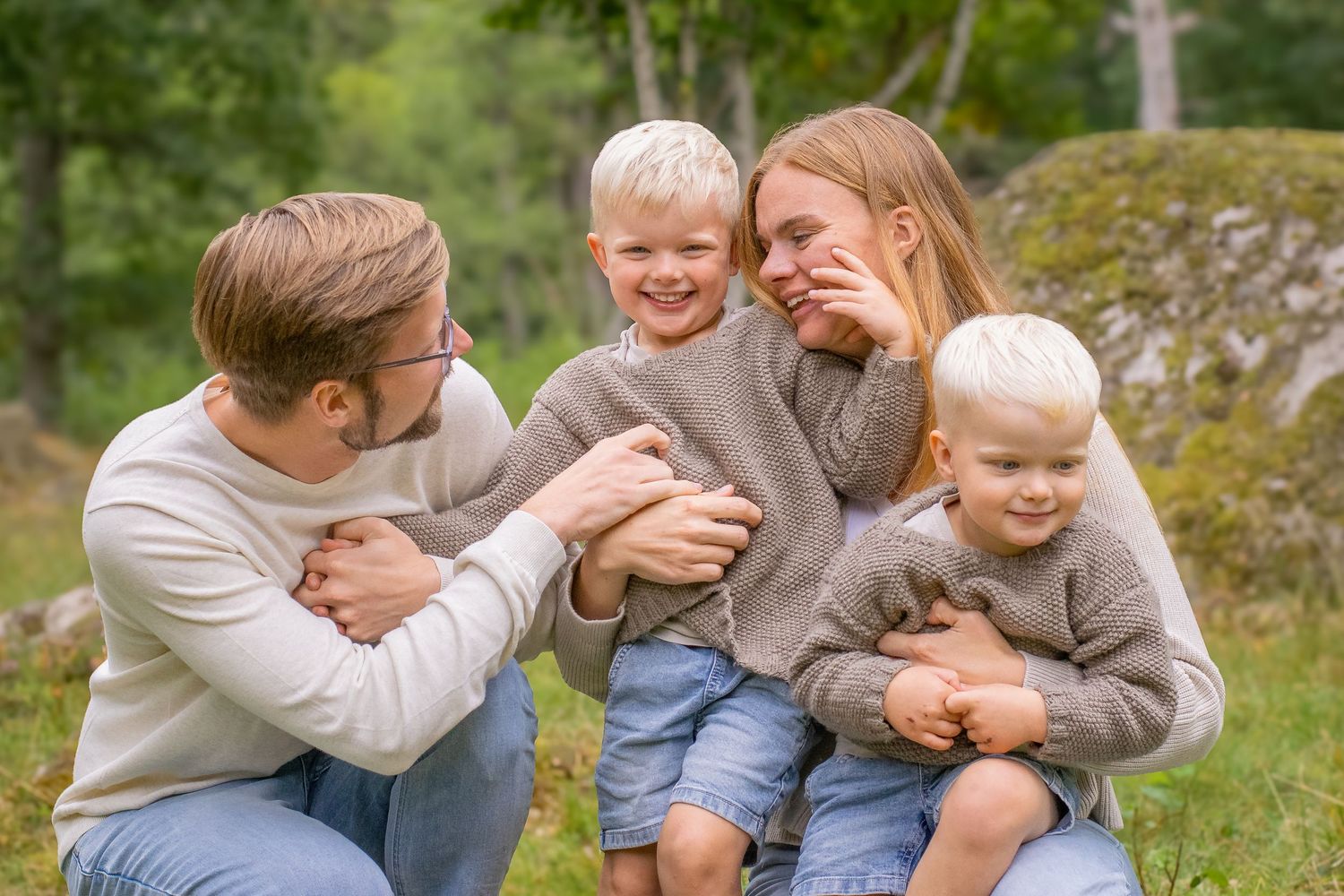 Ett pojke centrerad i bilden tittar rakt in i kameran och ler. Pappan sitter till vänster om pojken, och mamman med lillebror till höger.