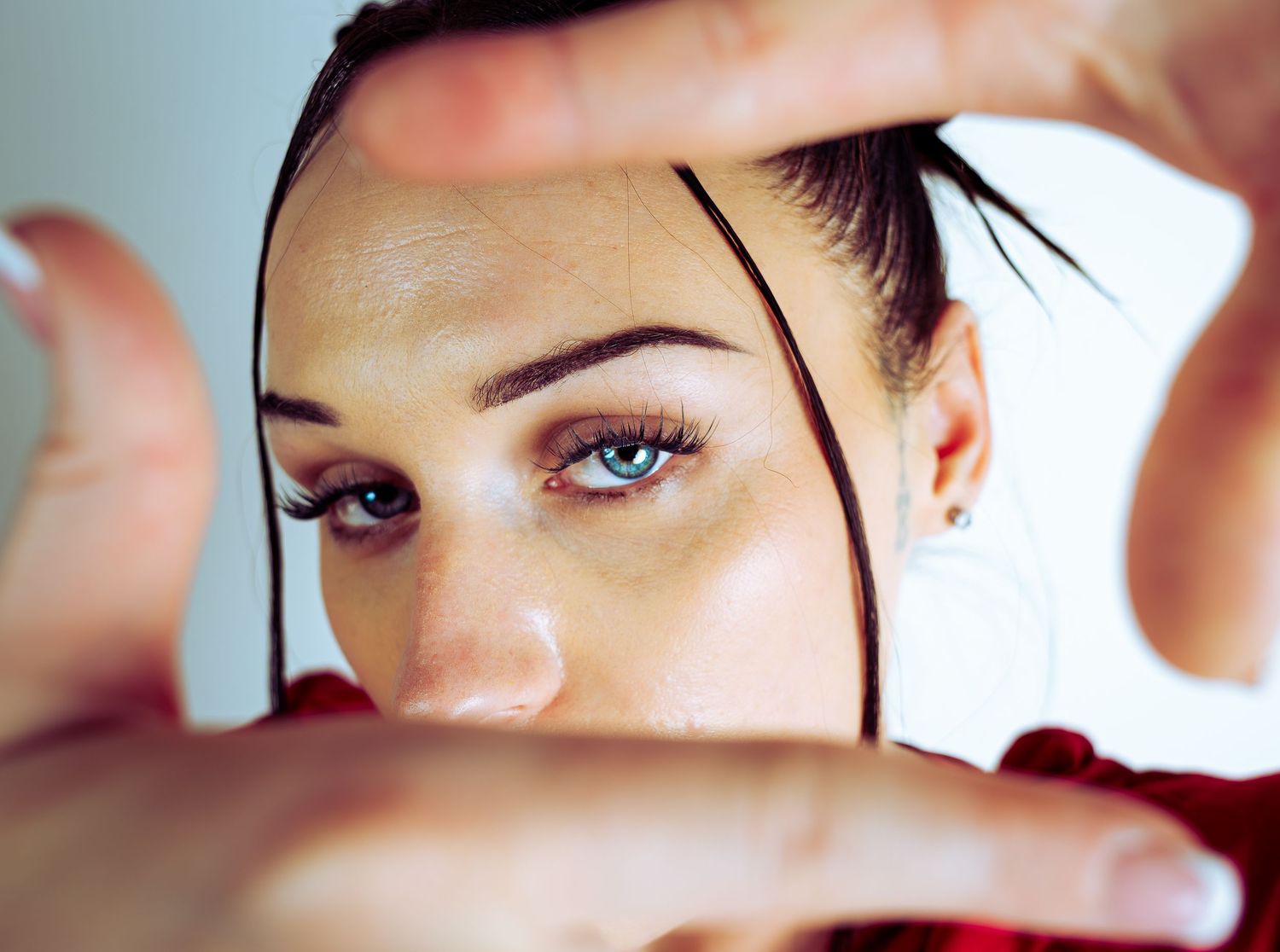 Close-up of a young woman framing her face with her hands, showcasing blue eyes and dark hair.
