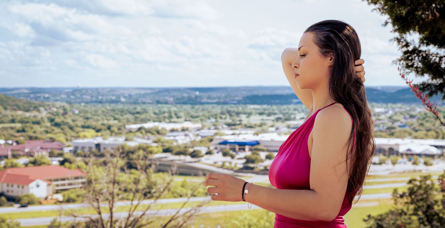 Woman in pink dress admiring panoramic city view from scenic hilltop lookout on a sunny day.