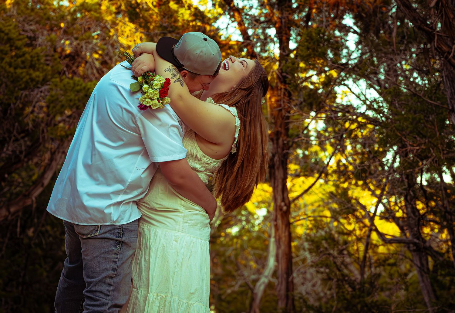 A couple embraces in a romantic outdoor setting during golden hour with sunlight filtering through trees.