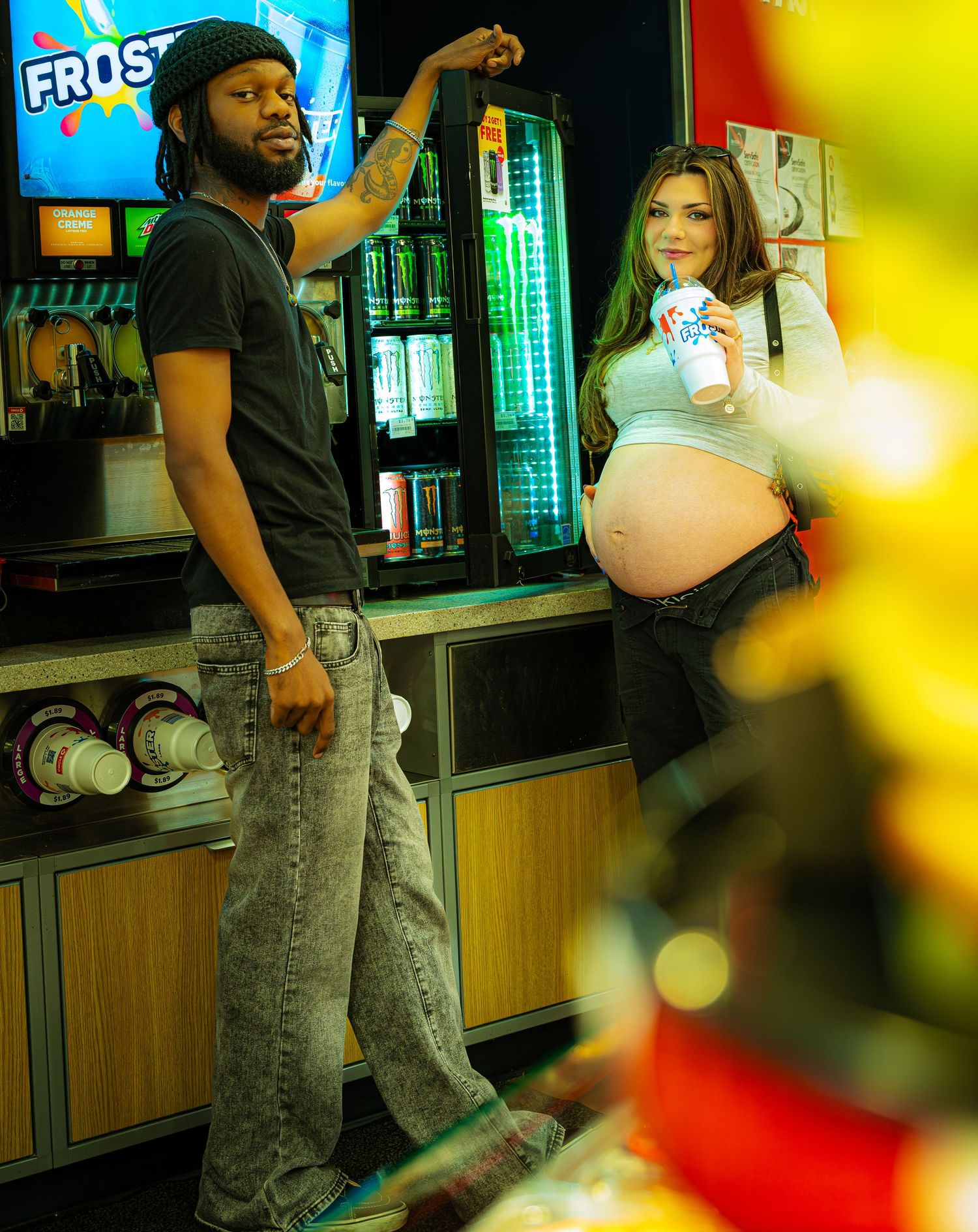 A couple stands at a convenience store counter with drinks and snacks in a colorful setting.