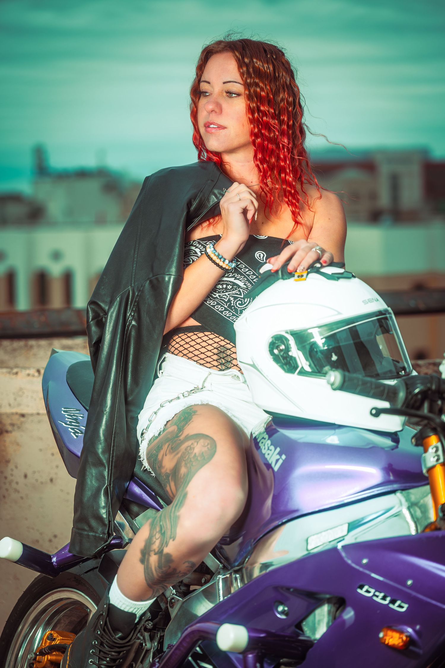 A motorcycle photoshoot featuring a purple and white sportbike with a model in a black jacket posing against a teal sky.