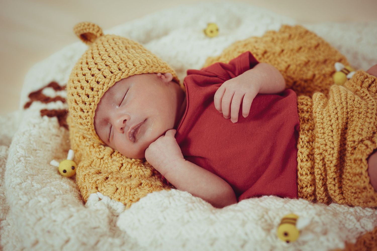 Newborn baby sleeping peacefully in a mustard yellow knit hat and blanket with a red onesie.